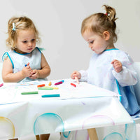 Girls drawing at table covered in messy mat