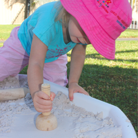 girl playing with wooden stamper in sand